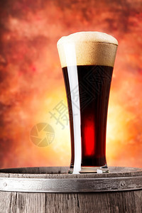 草案自然橙色背景中带泡沫和木桶的高杯黑啤酒带泡沫和木桶的高杯黑啤酒降低图片