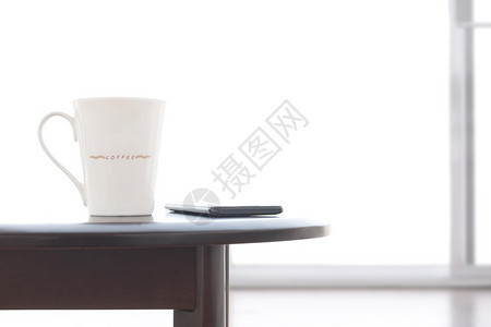 白色的电话陶瓷咖啡杯和智能手机紧贴在奥瓦尔木制桌上白色客厅有模糊的冰霜玻璃滑动门黑色的图片