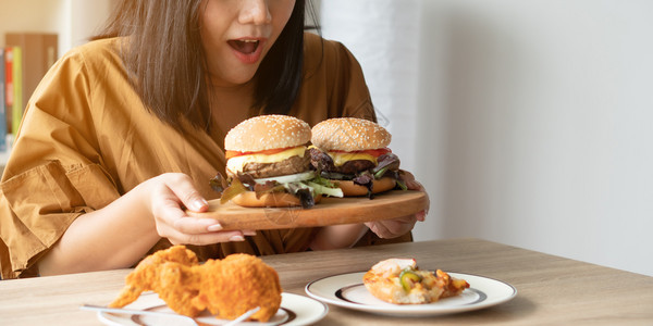 芝士汉堡饥饿的超重妇女在木板上拿着汉堡包炸鸡和餐桌上边子的披萨狂食饮紊乱概念BED年轻的肥胖图片
