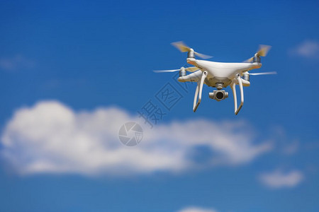 专业的摄像头无人驾驶飞机在清蓝的天空中飞行部分云彩笼罩清除白色的图片