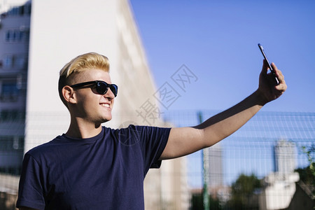现代的快乐蓝色带着太阳眼镜年轻男在户外自拍图片