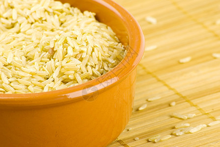 营养丰富在竹垫上的陶瓷碗中有机棕色长稻的种子图片