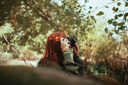 年轻女子用旧的模拟相机在森林里拍照千禧一代女士摄影师图片