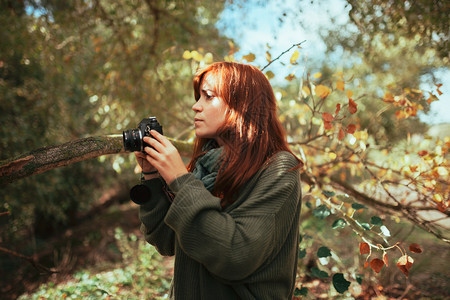 随意的户外年轻女子用旧的模拟相机在森林里拍照请享用图片