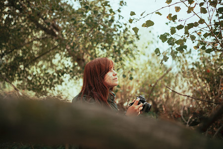 请享用老的照片年轻女子用旧的模拟相机在森林里拍照图片