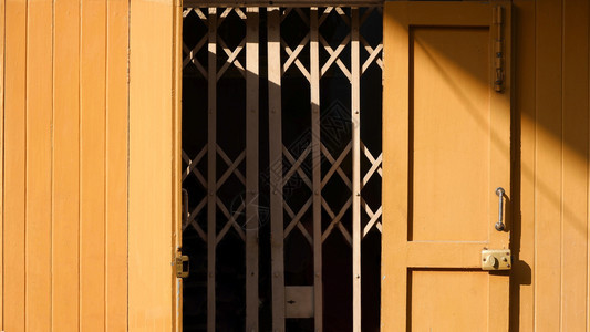 黄色木折叠门表面的阳光和阴影用古老的变形风格家庭外部建筑概念中的金属滑动门外部的屋闪亮图片