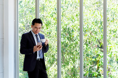 亚洲商人在办公室生活和商业概念中使用智能电话和喝咖啡亚洲商人使用智能电话沟通房间肖像图片