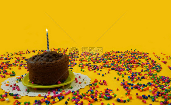 甜点巧克力生日蛋糕1个蓝色和白蜡烛在小绿色盘子上点亮周围是糖果球散布在黄色背景图象上有复制空间火焰白色的图片