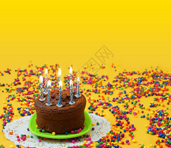 红色的小吃黄巧克力生日蛋糕8个蓝色和白蜡烛在绿的小盘子上点亮周围是黄色背景的糖果球图象有复制空间图片