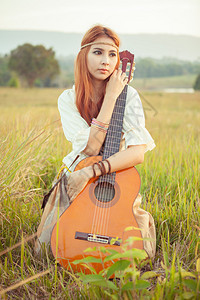 文化夏天户外美丽的乡村嬉皮女孩在草地上弹吉他图片