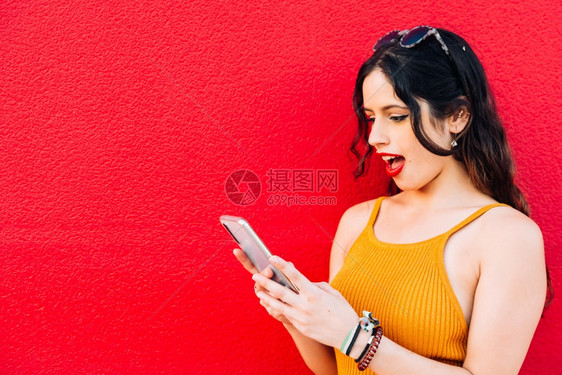 红色背景中张大嘴看着手机的女人红色背景中张开嘴看着手机的女人欣喜若狂应用程序宽的图片
