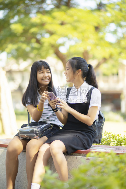 社会的微笑现代两个亚裔青少年的幸福面对着手握智能机的双口语低调放松情绪图片