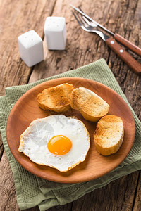 黄色的早午餐一个新鲜的煎蛋阳光明亮一面边上加烤包饼片放在木板餐具盐和胡椒在后面的选择焦点中专注鸡蛋前与烤面包白质图片