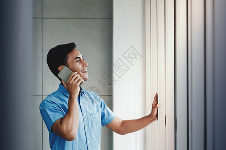 快乐的商人使用智能手机并站在办公室的窗口旁边通过移动电话外观与某人交谈107现代的复制讲话图片