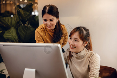 团队合作共同笑两个女商人在现代办公室计算机工作时以银幕为焦点的眼同事高兴的眼睛图片