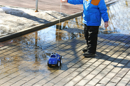 孩子在公园散步男孩翻滚着穿过一条绳子上的玩具车水坑户外熔化拉图片