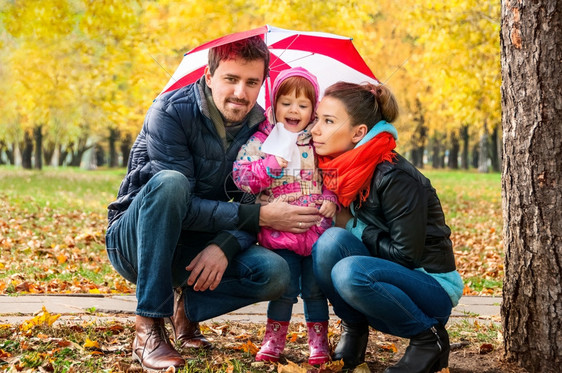 秋天公园的雨伞下快乐年轻家庭手母亲草地图片