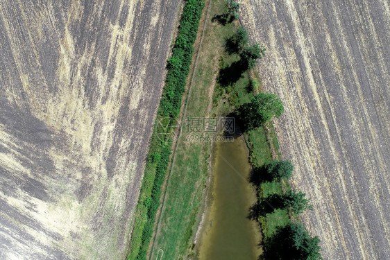 抽象的飞行天线从空中对一个渔池的角端进行摘要浏览该池在收获农田旁有一排树木图片