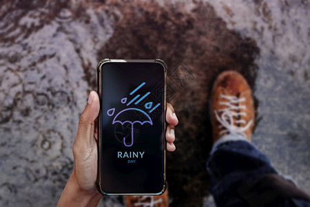 自然下雨男人通过移动电话在人行道上与伞状一起行走和看到天气预报的男日雨天概念图片