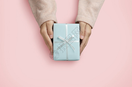 展示蓝色的女之手顶端视线拿着一个蓝色礼物盒在粉红色孤立的背景上平坦图片
