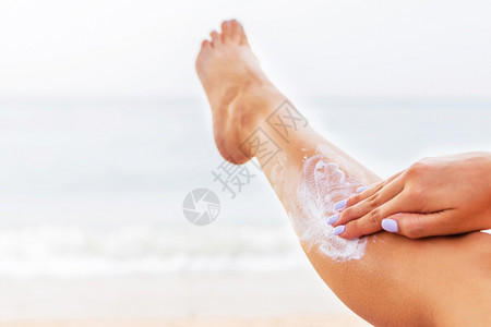海洋太阳的年轻女子在海滩的日光浴床上休息保护她的皮肤在腿上涂抹防晒霜海岸图片
