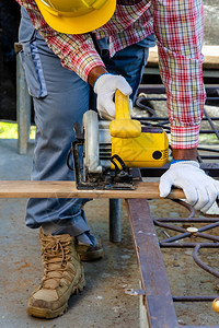 工人木匠佩戴安全头盔用手持的圆环砍木板看到伍德与人员保护概念一起工作户外锯图片