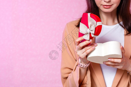 一个年轻的亚洲女孩拿着一个心形的礼物盒在一个粉红色孤立的背景里关注这个盒子复制女士幸福图片