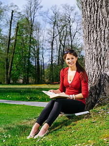 学生女孩放松一位美丽的年轻女子在早期春天A的一棵树旁阅读本书的照片图片
