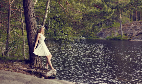 七月成人迷的年轻女子身着白夏洋服仰向松树阳光明媚的夏日湖底背景森林图片
