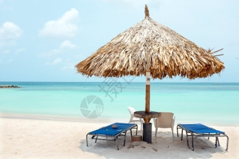 田园诗般的黄昏时阿鲁巴岛海滩的草伞阳蓝色图片
