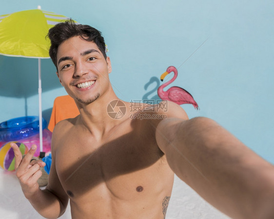 微笑的肌肉男在海滩上自拍享受帽子手机图片