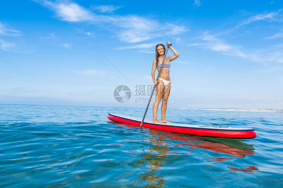 冲浪站立一个美丽的女人在阳光明媚的日子里练习划桨登机图片