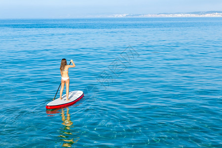支持一个美丽的女人在阳光明媚的日子里练习划桨海滩图片