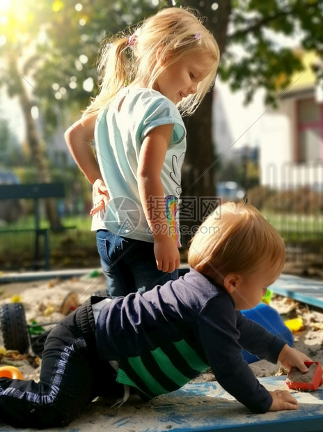 帮助好奇的姐妹和兄弟与在游乐场沙箱中相联的家庭一起玩沙的可爱小孩子在Sibbing休闲活动外一起玩游戏快乐照顾男孩的年长女童喜悦图片
