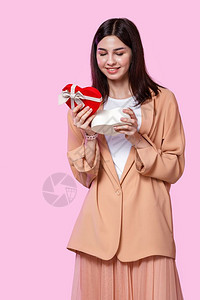 问候女使满意一个年轻女孩穿着蜜衣手里拿一个礼物盒的米色夹克在粉红孤立的背景下对礼物感到惊讶和满意图片