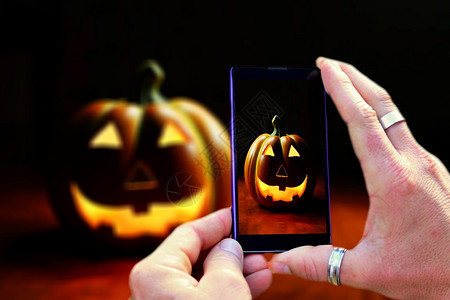 象征在拍摄Halloween南瓜时手握机和射杀Halloween南瓜移动电话屏幕视图笑有趣的图片