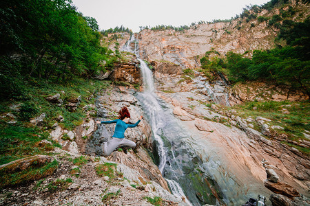 女孩夏天年轻子在瀑布附近的山上跳跃走图片