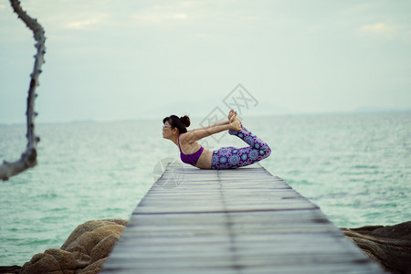 合身美丽的女人在海木码头做瑜伽在海龟上摆姿势漂亮的木制图片