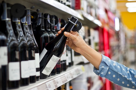 女人在超市背景买一瓶红酒的现在美食超级市场图片