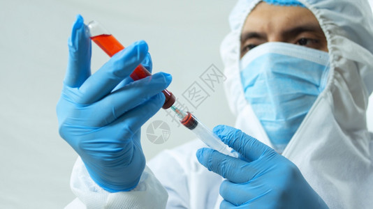 身穿生物防护服面罩和蓝色手套的拉丁医生在白色背景上用注射器在试管中抽取血液样本的特写视图身穿生物防护服面罩和蓝色手套的拉丁医生从图片