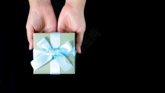 手拿着一件小礼物包裹着黑色背景的蓝丝带女弓女士图片