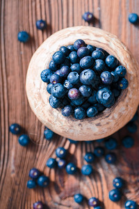 木头将新收集的蓝莓放入旧陶瓷碗中一些水果自由散落于老木板桌上新鲜维他命图片