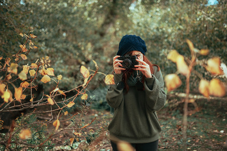 徒步旅行者年轻女子用旧的模拟相机在森林里拍照年轻的豆图片