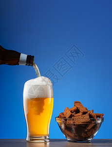 盐黑麦饼干和啤酒倒在玻璃杯上放蓝底的盐黑麦饼干和倒入玻璃中的啤酒上液体精辛辣的图片