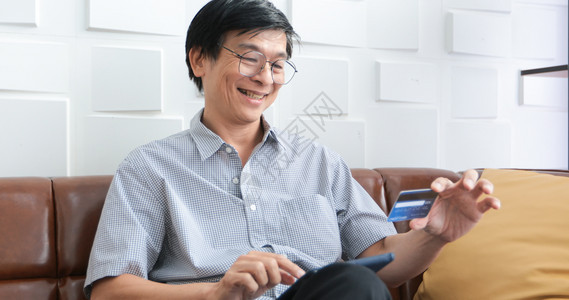 卡片高级亚洲男子在网上使用智能电话购物并在家里用信卡支付费在室内白色的图片