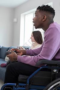 白种人包容坐在轮椅上与Frend在家玩电脑视频游戏的青少年男孩图片