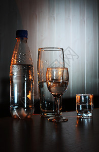 透明瓶子和一杯水在黑暗背景上带光的暗底面玻璃一种图片