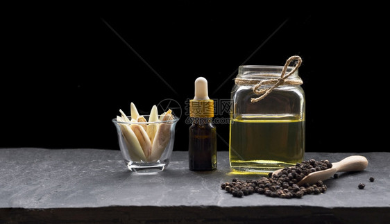 结石在玻璃罐和柠檬草中装有药基本油的瓶子在玻璃罐和柠檬草中装有油在小玻璃中切片在深底黑色板块上的木勺装黑胡萝子液体种图片
