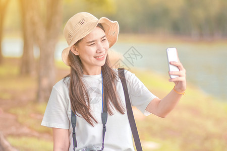 相机摆姿势微笑带智能电话旅行的美女自拍相片图片