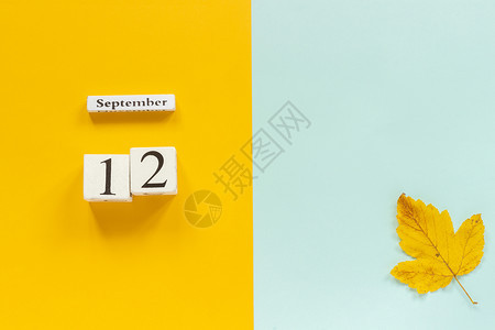 时间黄色的躺着秋季作文木制日历9月12日和黄色蓝背景上的黄秋叶顶视图平躺样机概念你好月秋季作文木制日历图片
